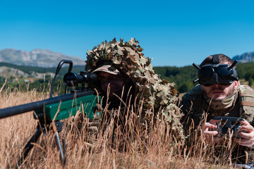 Obraz premium Sniper soldier assisted by an assistant to observe the area to be targeted with modern warfare tactical virtual reality goggles aerial drone military technology.