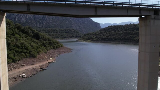 Establishing shot of vehicles passing on bridge over river, interconnecting huge mountains. Aerial.