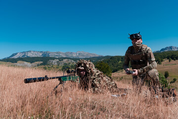 Sniper soldier assisted by an assistant to observe the area to be targeted with modern warfare tactical virtual reality goggles aerial drone military technology. - obrazy, fototapety, plakaty