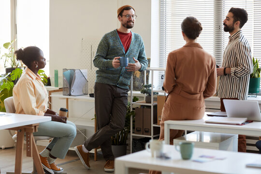 Group Of Four Young Intercultural Managers Discussing Latest News Or Plans For Following Weekend While Having Coffee At Break