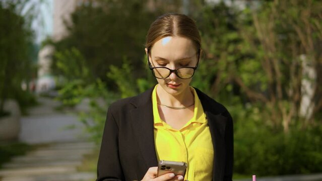 Office Worker Female Adult Looking At Phone Screen Using Smartphone Standing In A Park On Summer Day - Portrait Front View