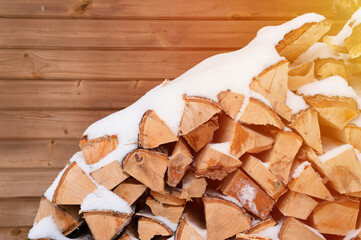 textured firewood background chopped wood for kindling. woodpile with stacked firewood birch tree covered fresh icy frozen snow and snowflakes. cold weather and snowy winter time season. flare