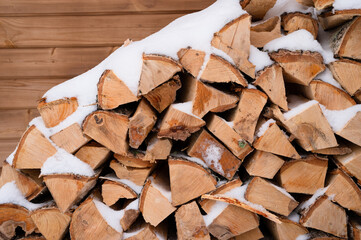 textured firewood background chopped wood for kindling and heating. woodpile with stacked firewood birch tree covered fresh icy frozen snow and snowflakes. cold weather and snowy winter time season