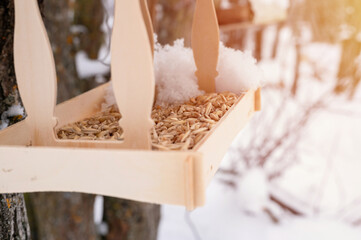 wooden feeder for wild forest birds with food hanging on tree covered with fresh frozen snow and snowflakes on frosty winter day in forest or garden. animal care. snowy winter season in nature. flare