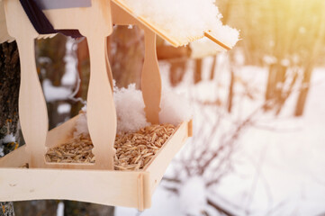 wooden feeder for wild forest birds with food hanging on tree covered with fresh frozen snow and snowflakes on frosty winter day in forest or garden. animal care. snowy winter season in nature. flare