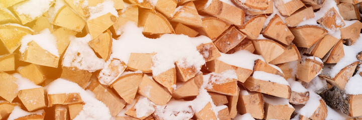 textured firewood background chopped wood for kindling. woodpile stacked firewood birch tree covered fresh icy frozen snow and snowflakes. cold weather and snowy winter time season. banner. flare