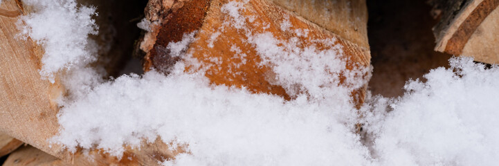 textured firewood background chopped wood for kindling and heating. woodpile stacked firewood birch tree covered fresh icy frozen snow and snowflakes. cold weather and snowy winter time season. banner