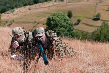 Sniper soldier assisted by an assistant to observe the area to be targeted with modern warfare tactical virtual reality goggles aerial drone military technology.