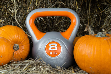 Heavy kettlebell and orange pumpkins on the hay. Healthy fitness lifestyle autumn fall composition for Halloween or Thanksgiving. Gym workout and sport training concept on a pumpkin patch farm. - Powered by Adobe
