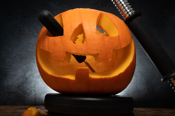 Carved Halloween pumpkin head Jack-o'-lantern with dumbbell barbell weight plates and carving...
