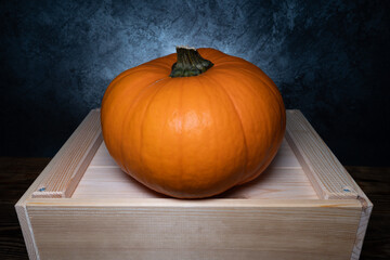 Orange pumpkin with stem cut off, autumn or fall still life on a wooden box.