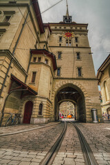 Tram railway tunnel under the baroque tower Kafigturm above a old historical cobbled street. Cablecar track or tracks across the arched medieval steeple in the popular Marktgasse. Bern, Switzerland