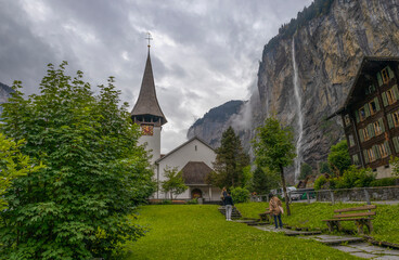 Fototapeta na wymiar LAUTERBRUNNEN, SWITZERLAND, JUNE 22, 2022 - The church in the alpine town of Lauterbrunnen with the The Staubbach waterfall, in Bernese Oberland, Switzerland.
