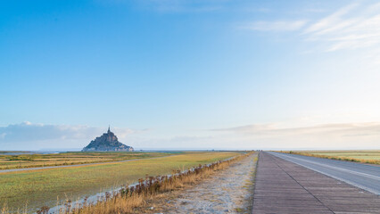 The road leading to the famous Mont Saint Michel, Normandy, France. Big yellow field during low...