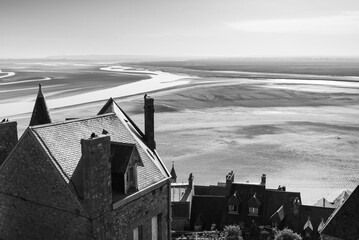 Aerial view of the coastline of the Normandy, France, from the walls of the famous Mont Saint Michel. Stone corridor on the right. The coastline during low tide on the left. Monochromatic.