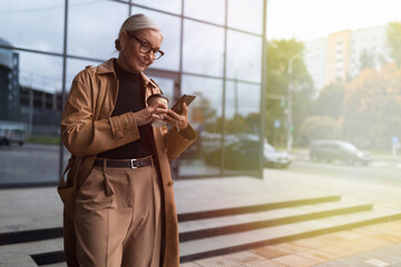 mature businesswoman with a mobile phone on the background of an office building, woman leader in business concept