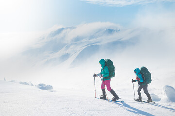 two girls with a backpack and snowshoes walk in the snow during a snow storm.