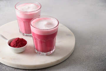 Beetroot latte or pink moon milk latte in glasses of beetroot powder and vegan milk on gray background. Trendy healthy vegan drink. Close up. Copy space.