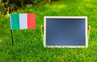 black blank chalk board and flag of Italy on green lawn. place for text, copy space.