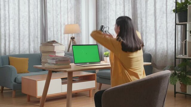 Side View Of A Young Female Raising Her Hand For Celebrating Succeed Using Mock-Up Green Screen Laptop While Studying At Home
