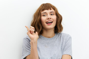 a funny, emotional, beautiful woman smiles broadly and gestures with her fingers towards an empty space on the background for inserting an advertising layout