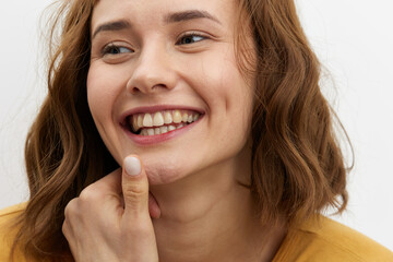 Fototapeta premium a happy, joyful woman stands on a white background in a yellow T-shirt playfully holding her finger near her mouth