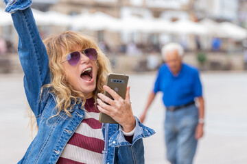 middle-aged woman excited with joy on the street with mobile phone