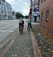 A man and a woman from the back (face not visible) on bicycles stand at a traffic light waiting for a green signal in autumn