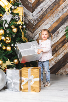 Little Girl Holding Big Wrapped Present Standing Beside Decorated Christmas Tree On Boxing Day