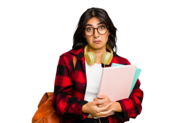 Young student Indian woman wearing headphones isolated shrugs shoulders and open eyes confused.