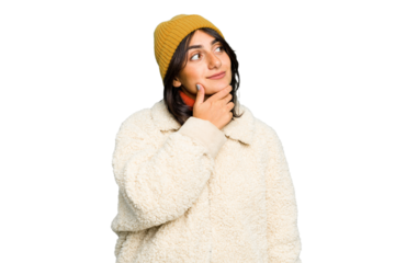 Young Indian woman wearing winter jacket and a wool cap isolated looking sideways with doubtful and skeptical expression.