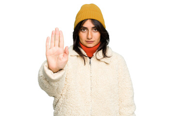 Young Indian woman wearing winter jacket and a wool cap isolated standing with outstretched hand showing stop sign, preventing you.