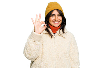 Young Indian woman wearing winter jacket and a wool cap isolated cheerful and confident showing ok gesture.