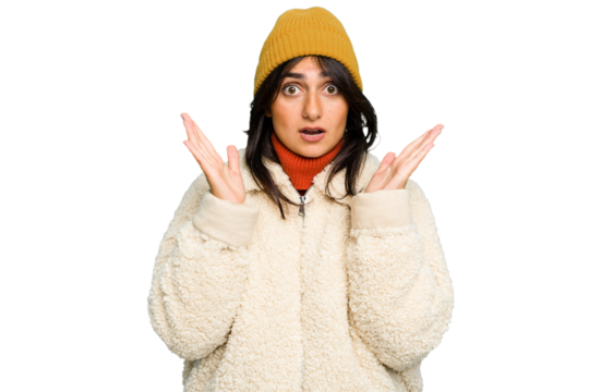 Young Indian woman wearing winter jacket and a wool cap isolated surprised and shocked.