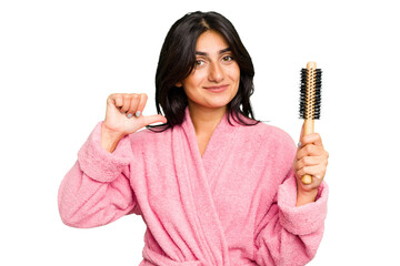 Young Indian woman in a bathrobe holding an hairbrush isolated feels proud and self confident,...