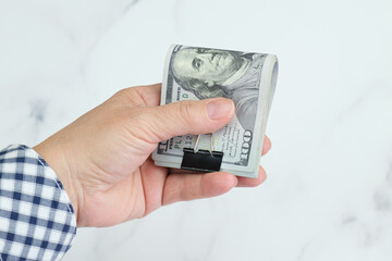 Elderly woman holding Stack of one hundred dollar bills folded in half and secured with a metal clip on a white background. Financial concept, savings.