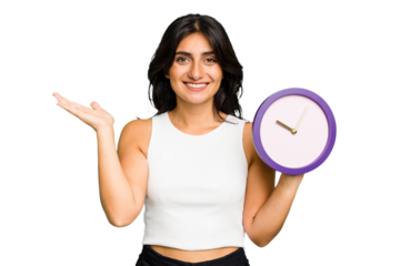 Young Indian woman holding a clock isolated showing a copy space on a palm and holding another hand on waist.
