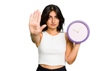 Young Indian woman holding a clock isolated standing with outstretched hand showing stop sign, preventing you.