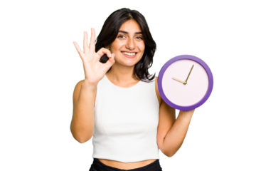 Young Indian woman holding a clock isolated cheerful and confident showing ok gesture.