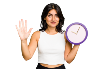 Young Indian woman holding a clock isolated smiling cheerful showing number five with fingers.