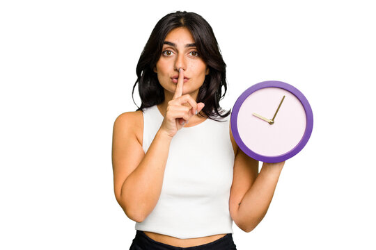 Young Indian woman holding a clock isolated keeping a secret or asking for silence.