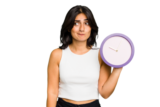 Young Indian woman holding a clock isolated confused, feels doubtful and unsure.