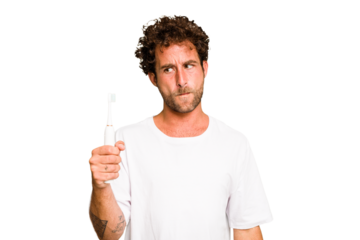 Young caucasian man holding an electric toothbrush isolated confused, feels doubtful and unsure.