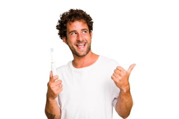 Young caucasian man holding an electric toothbrush isolated points with thumb finger away, laughing and carefree.
