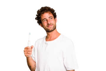 Young caucasian man holding an electric toothbrush isolated looks aside smiling, cheerful and pleasant.