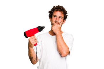 Young caucasian man holding an hairdryer isolated looking sideways with doubtful and skeptical expression.
