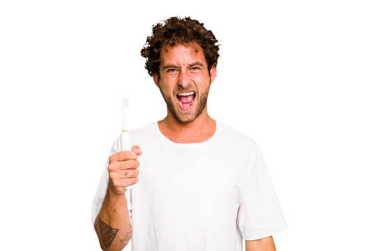 Young caucasian man holding an electric toothbrush isolated screaming very angry and aggressive.