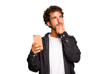 Young caucasian man using mobile phone isolated looking sideways with doubtful and skeptical...
