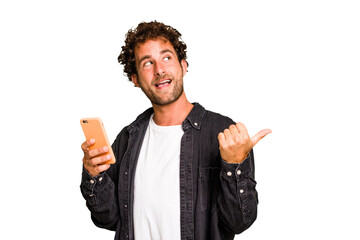Young caucasian man using mobile phone isolated points with thumb finger away, laughing and...