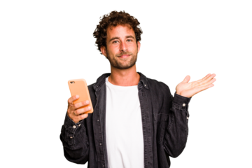 Young caucasian man using mobile phone isolated showing a copy space on a palm and holding another hand on waist.